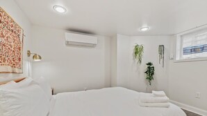 A modern bedroom with a large bed, an air conditioning unit, a wall-mounted lamp, and a window with a view.