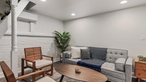 A modern living room with a grey sofa, wooden chairs, a coffee table, and a staircase.
