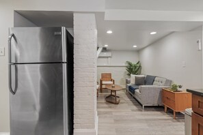 Une cuisine moderne avec un réfrigérateur en acier inoxydable, un meuble en bois et un canapé gris dans l’espace salon.