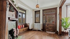 Ein geräumiges Entree mit Holzboden, einer Bank mit bunten Kissen, einem Kamin und einer großen Holztür mit der Nummer 30.