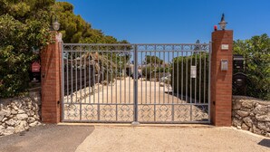 Ein verschlossener Eingang mit einer Ziegelmauer und einem Metallgitter, umgeben von Grünpflanzen und blauem Himmel.