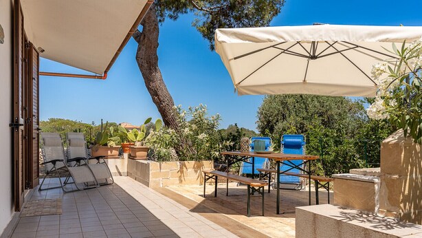 Eine Terrasse im Freien mit Lounge-Möbeln, einem Tisch und einem großen Sonnenschirm.