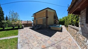 Une terrasse en pierre avec une piscine, un petit espace salon extérieur et un bâtiment à la façade en pierre.