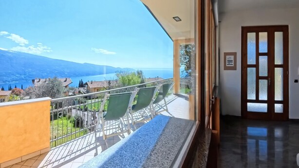 Un balcon donnant sur un lac et des montagnes, une porte avec des panneaux en verre dépoli et un sol carrelé.