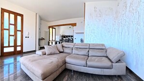 Un salon moderne avec un grand canapé d’angle, une cuisine en arrière-plan et un mur orné d’un motif.