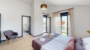 A modern bedroom with a large bed, a chair, a bathroom with a mirror, and a view of the outside. - Villa Silvia in Mihatovici (Mihatovici)