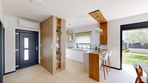 A modern kitchen with a central island, a dining area with two white chairs, and a large window overlooking a garden. - Villa Silvia in Mihatovici (Mihatovici)