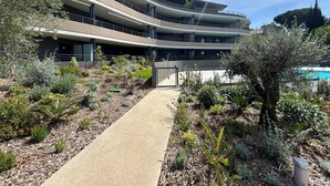 A multi-story building with a central courtyard, surrounded by various plants and a pathway leading to the entrance.