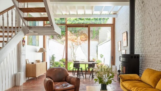 A spacious living area with a wooden staircase, a leather armchair, a yellow sofa, and a fireplace. - Architect Garden House (Brussels)