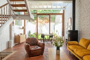 A spacious living area with a wooden staircase, a leather armchair, a yellow sofa, and a fireplace.