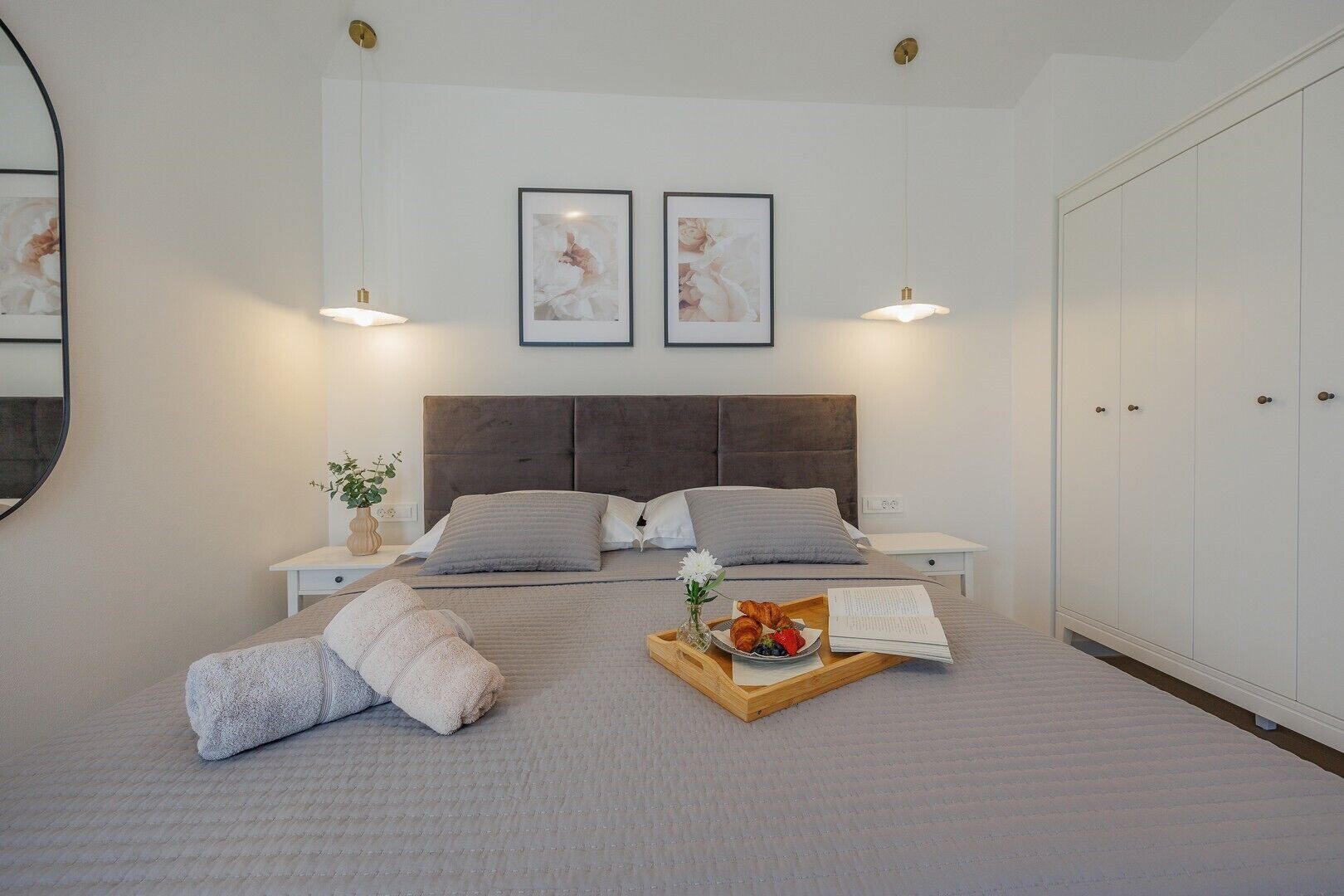 A neatly arranged bedroom with a large bed, two bedside tables, a bedside lamp, a wooden tray with breakfast items, and a wardrobe.