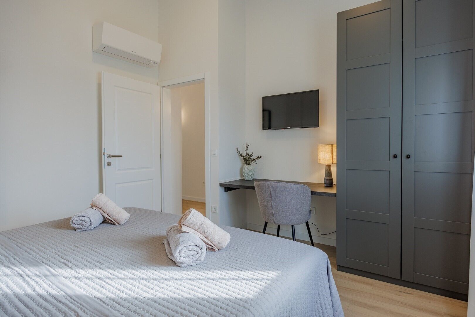 A bedroom with a bed, a desk, a chair, a TV, and a wardrobe.