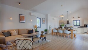 A spacious living area with a sofa, a dining table, and chairs. There is a kitchen in the background with modern appliances. - Luxury Villa Oliva Oliana heated pool 32m2, bbq, family (Vrsi)