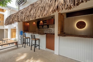 A bar area with a thatched roof, wooden stools, and a water dispenser. - The Circle Hostel (San Juan)