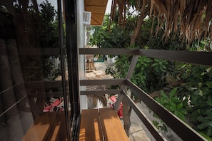 A wooden bench with a view of a garden area, including a thatched structure and a red bicycle. - The Circle Hostel (San Juan)