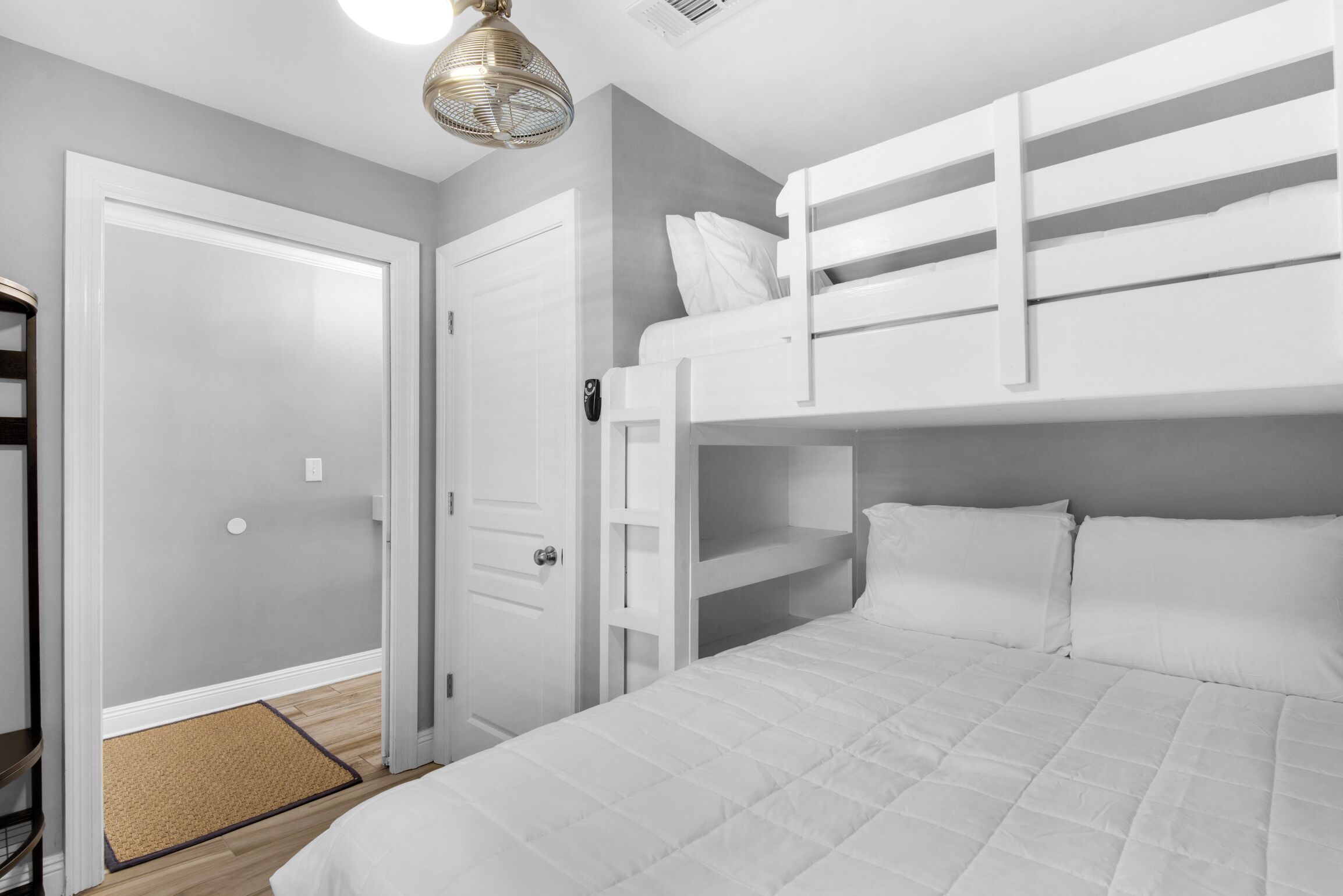 A room with a bunk bed, a door, a bedside table, and a hanging light fixture.