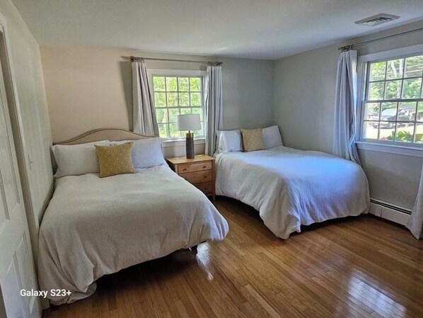 A hotel room with two beds, a nightstand with a lamp, and a window with curtains.