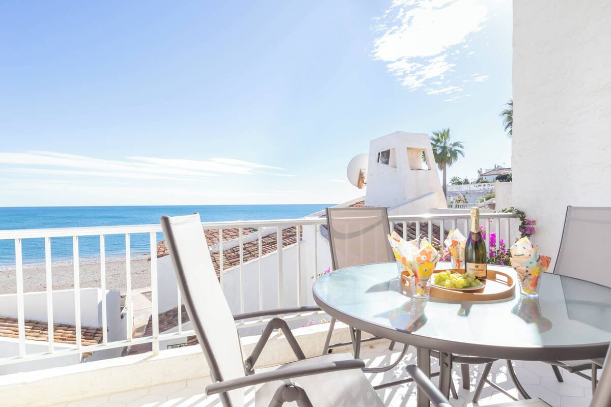 A balcony with a glass table, chairs, and a bottle of champagne.