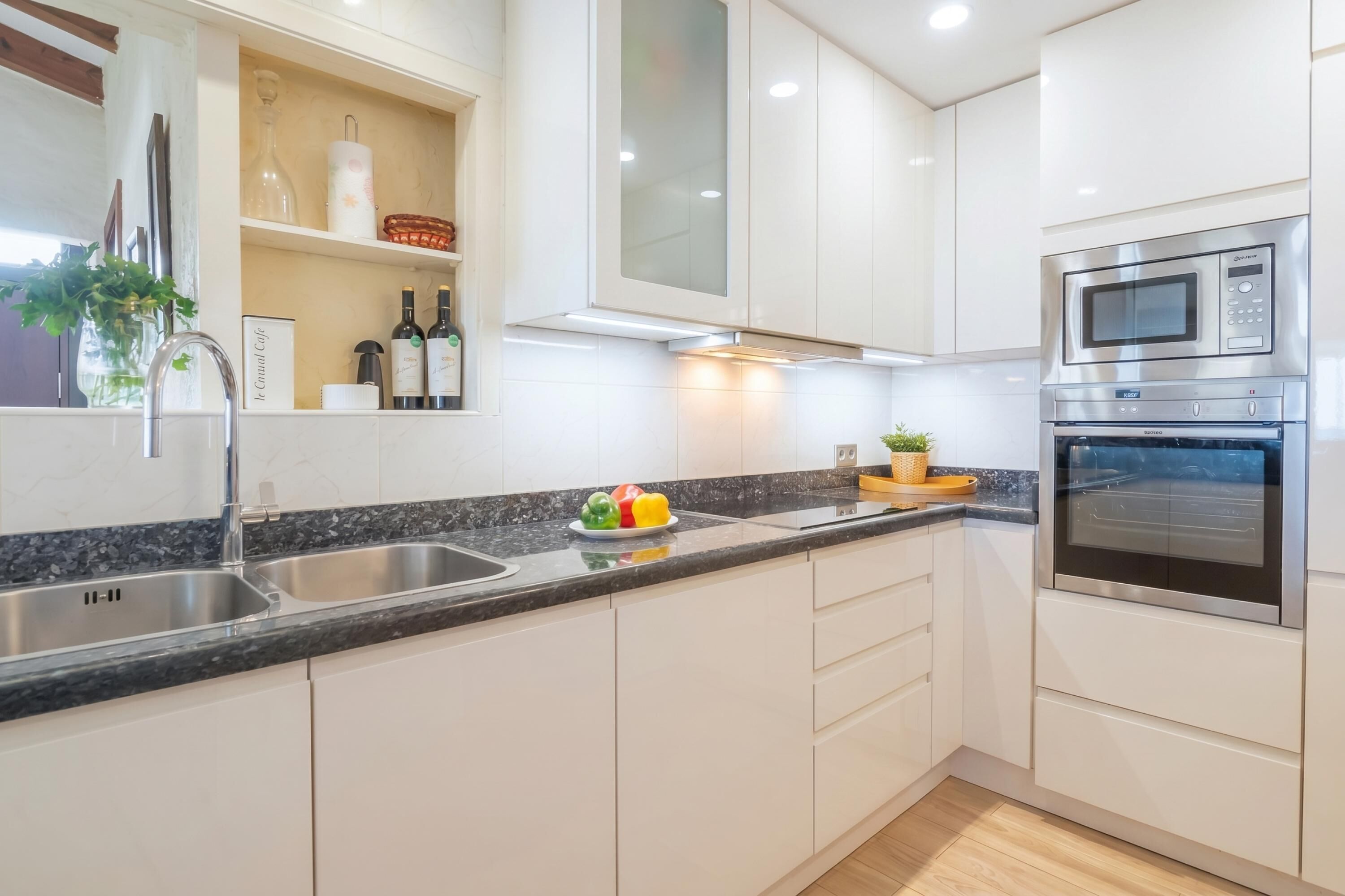 A modern kitchen with white cabinets, a stainless steel sink, a microwave, and an oven.