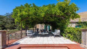 Eine Terrasse mit Gartenmöbeln, einer Steinmauer und einem Gebäude mit grünen Fensterläden.