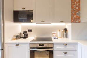 A modern kitchen with white cabinetry, a built-in microwave, a coffee machine, and a dishwasher.