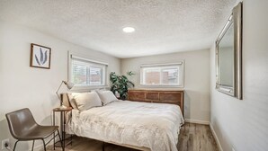 Een slaapkamer met een bed, nachtkastje, stoel en een grote spiegel.