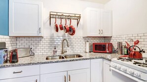 A kitchen with white cabinets, a granite countertop, a stainless steel sink, a red microwave, a gas stove, and hanging pots. - Nob Hill Haven, near UNM (Albuquerque)