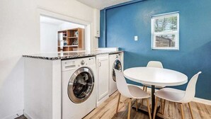A compact kitchen with a washing machine, a dining table with chairs, and a blue accent wall. - Nob Hill Haven, near UNM (Albuquerque)