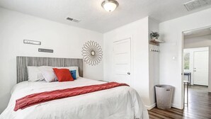 A bedroom with a bed, a wall-mounted decorative piece, a door, and a trash can. - Nob Hill Haven, near UNM (Albuquerque)