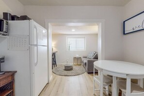 Een compacte keuken met een witte koelkast, een koffieapparaat en een klein eetgedeelte met een ronde tafel en stoelen.