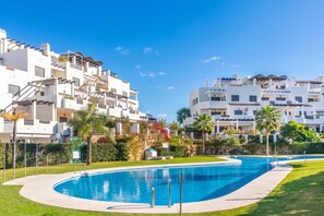 A swimming pool surrounded by white buildings with balconies, palm trees, and a clear blue sky. - Sunset Golf Elegance (Estepona)
