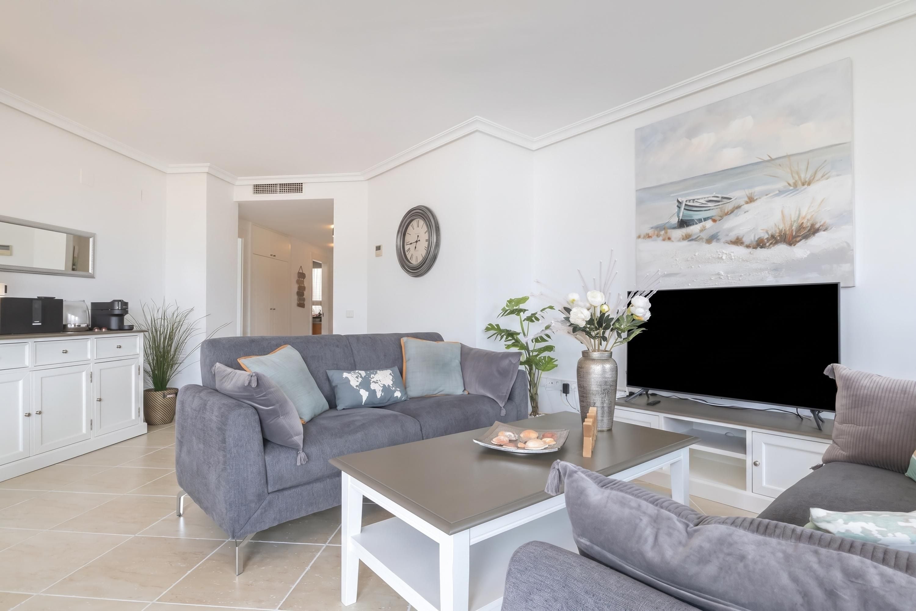 Un salon moderne avec un canapé gris, une table basse, un téléviseur à écran plat et un tableau accroché au mur.