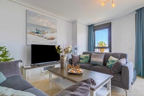 A modern living room with a flat-screen TV, a sofa set, a coffee table, and a painting on the wall. - Sunset Golf Elegance (Estepona)