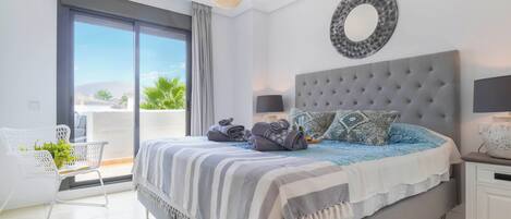 A bedroom with a large bed, a round mirror, a bedside table with a lamp, and a view of the outdoors through a sliding door.