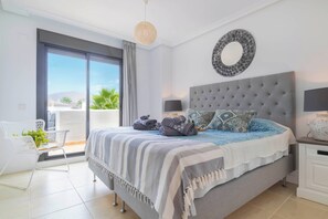 Une chambre avec un grand lit, un miroir rond, une table de chevet avec une lampe, et une vue sur l’extérieur grâce à une porte coulissante.