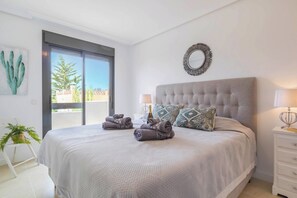 A bedroom with a large bed, a nightstand, a mirror, and a view of the outdoors. - Sunset Golf Elegance (Estepona)