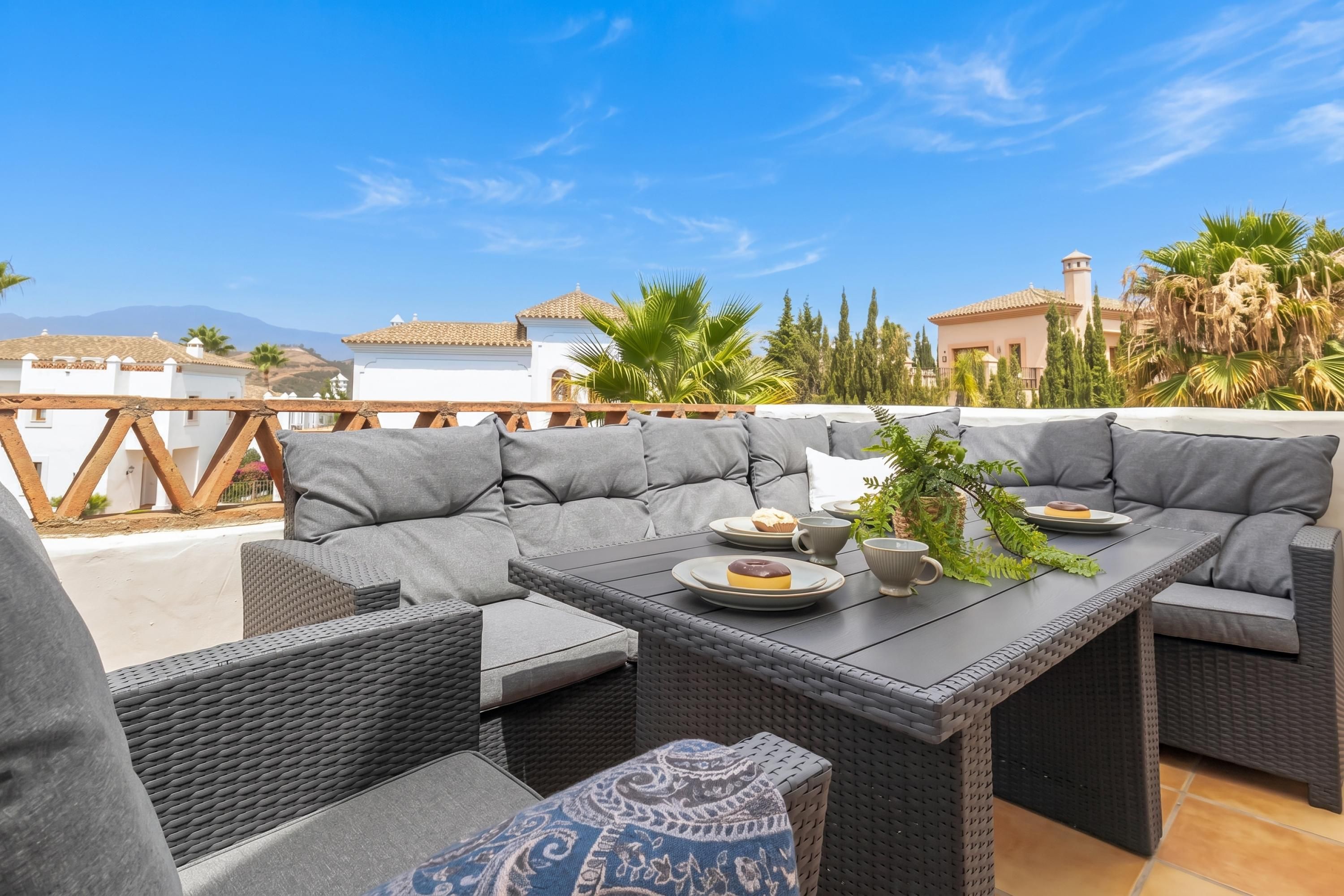 A rooftop patio with a sectional sofa, a dining table, and a view of the surrounding landscape.
