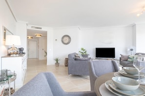 A modern living room with a sofa, TV, and dining area with plates and a glass. - Sunset Golf Elegance (Estepona)