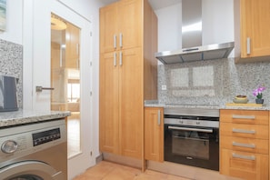 A compact kitchen with wooden cabinets, a built-in oven, and a washing machine. - Sunset Golf Elegance (Estepona)