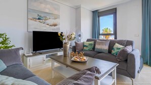 A modern living room with a flat-screen TV, a sofa set, a coffee table, and a painting on the wall. - Sunset Golf Elegance (Estepona)
