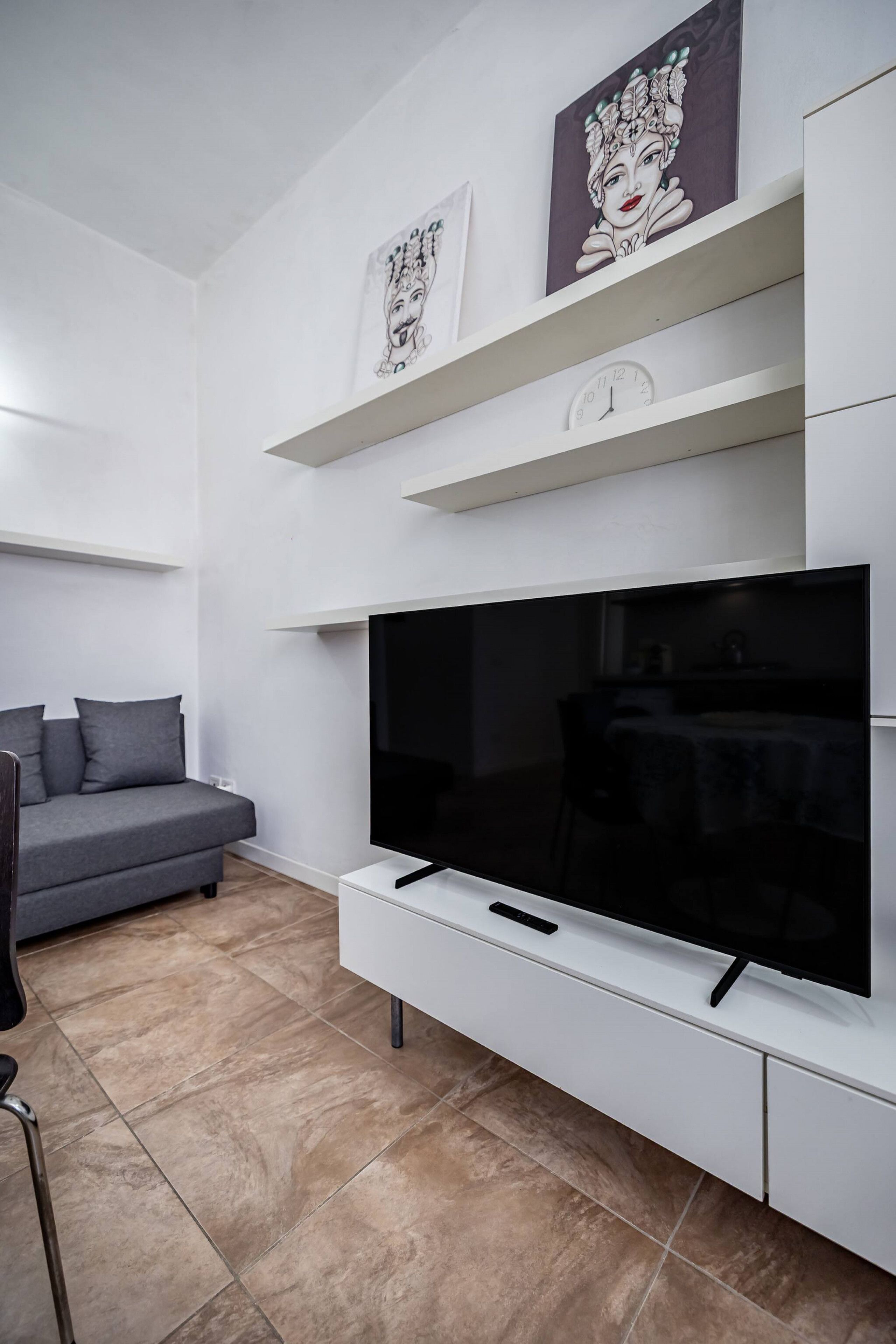 Een moderne woonkamer met een flatscreen televisie, een grijze bank en kunstwerken aan de wanden.