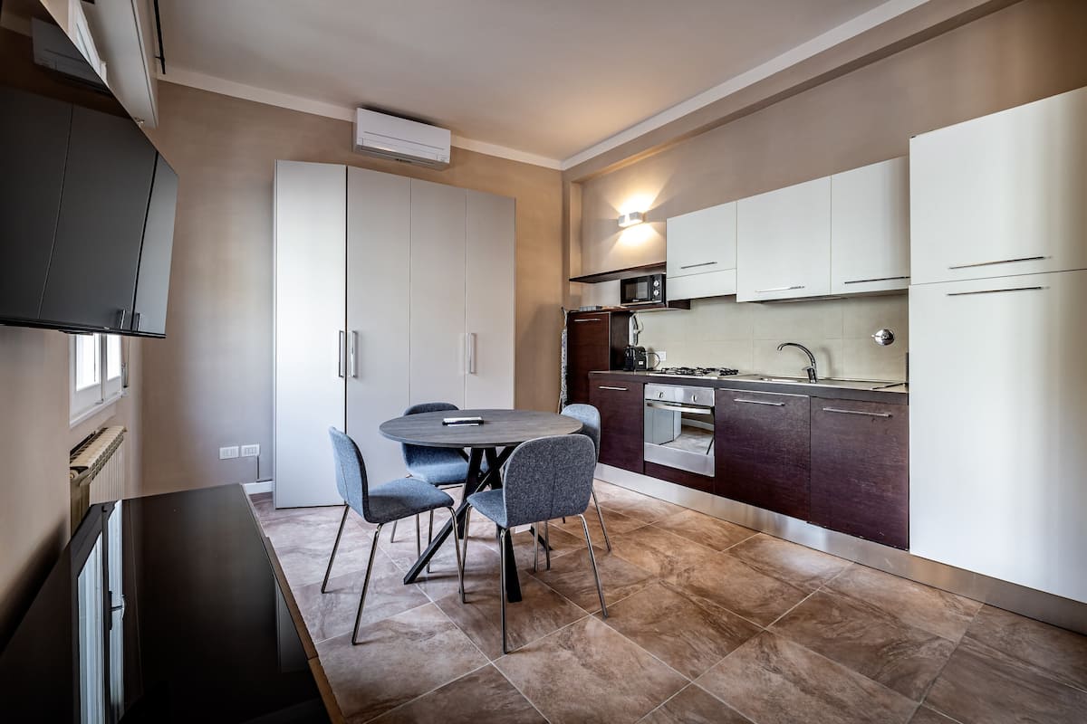 A compact kitchen with a dining area, featuring modern appliances, a built-in oven, and a dining table with chairs.