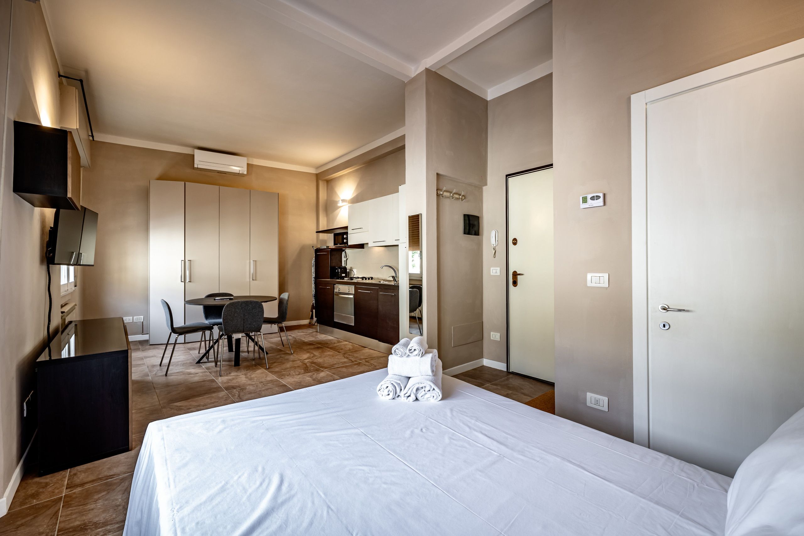 A hotel room with a bed, a desk, a chair, a kitchenette, and a bathroom.