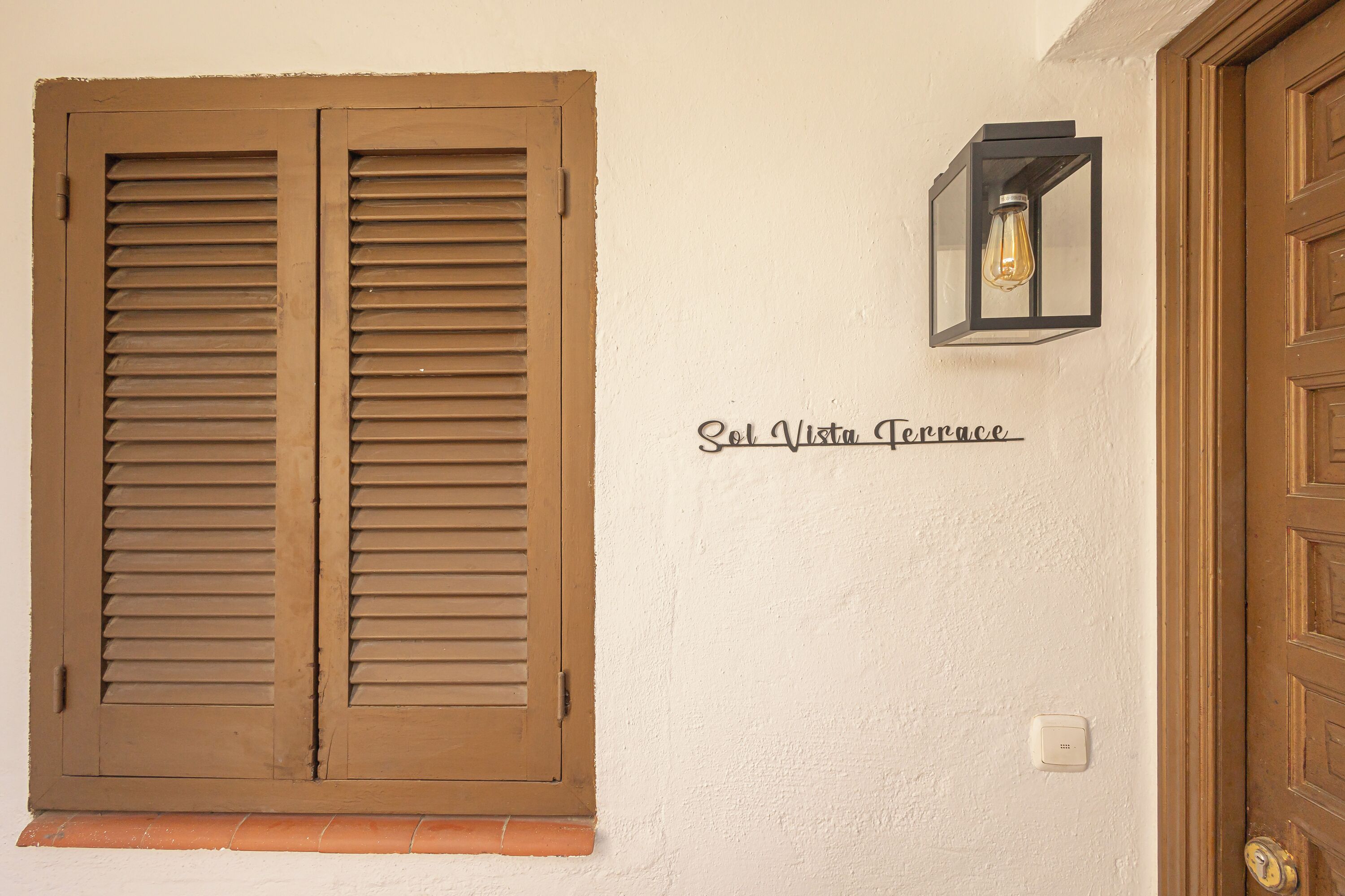 A wooden door, a window with shutters, and a wall-mounted light fixture.