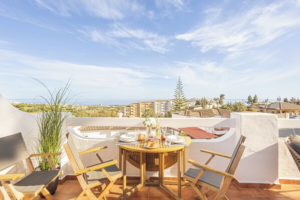 A terrace with a table set for dining, overlooking a coastal view.