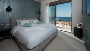 Un dormitorio moderno con una cama grande, vistas a la playa y un balcón con mobiliario exterior.