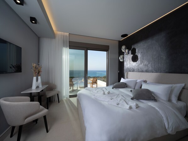 Une chambre d’hôtel moderne dotée d’un grand lit, d’un bureau, d’une chaise, d’une télévision et d’un balcon offrant une vue sur la mer.