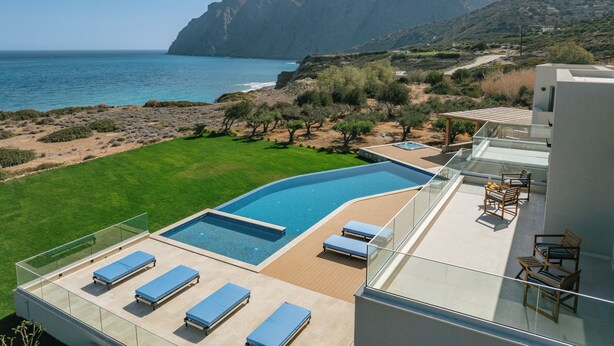 Una villa moderna con piscina en la azotea, sillones de descanso y vistas al mar y a las montañas.