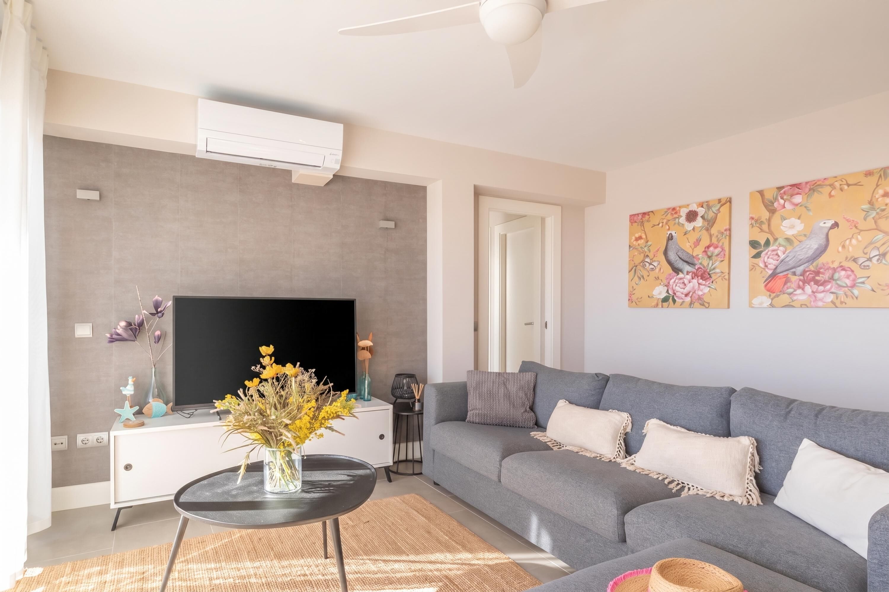Un salon moderne avec un canapé gris, un téléviseur à écran plat, un meuble blanc et des œuvres d’art décoratives au mur.