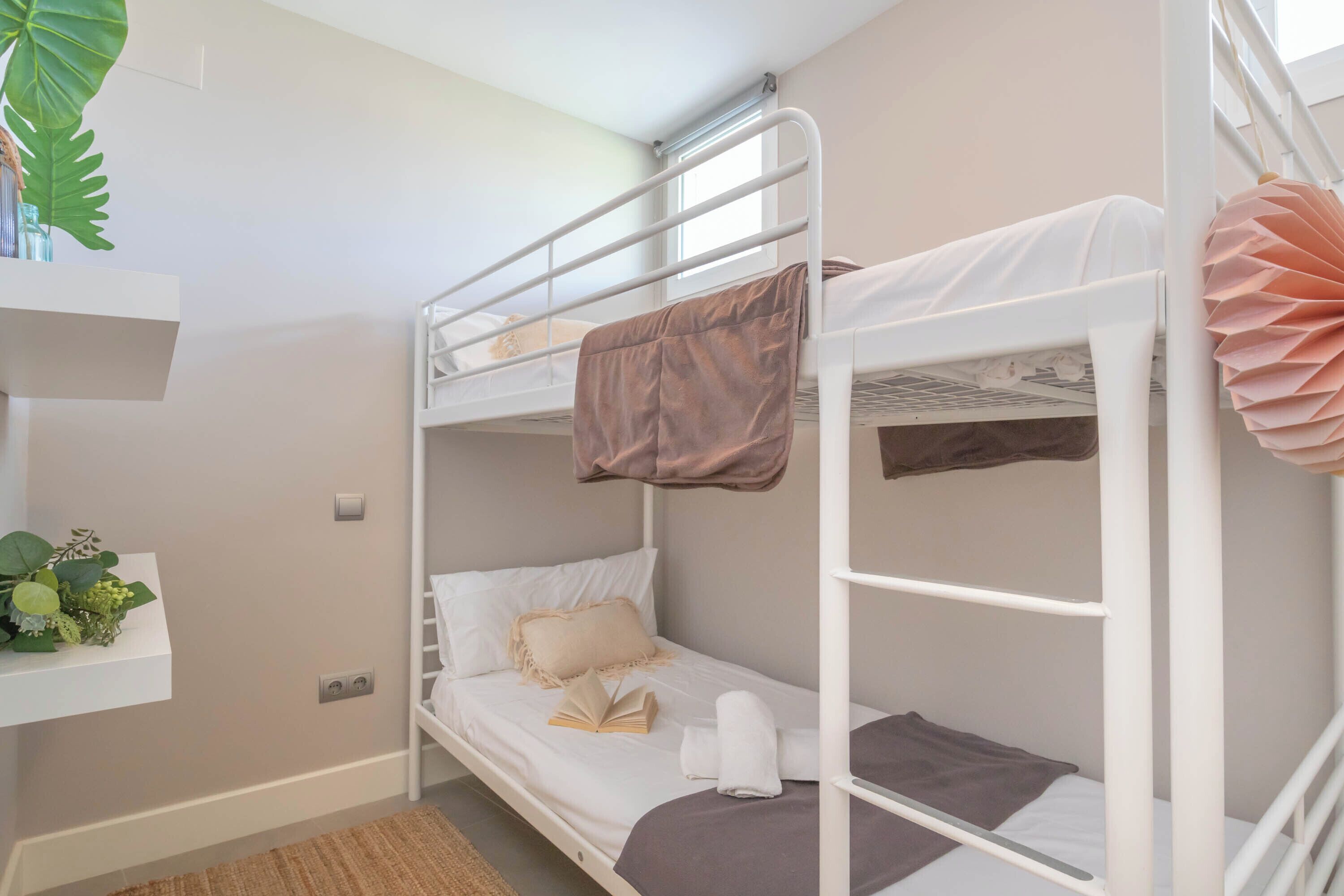 A bunk bed room with a shelf above the lower bunk, a plant on the shelf, and a window with blinds.